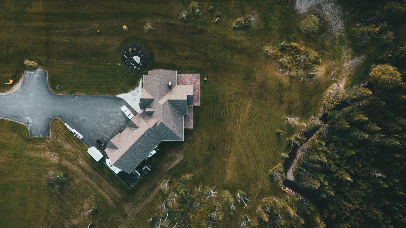 Flyfoto av et bolighus med innkjørsel, omgitt av jorder og skog