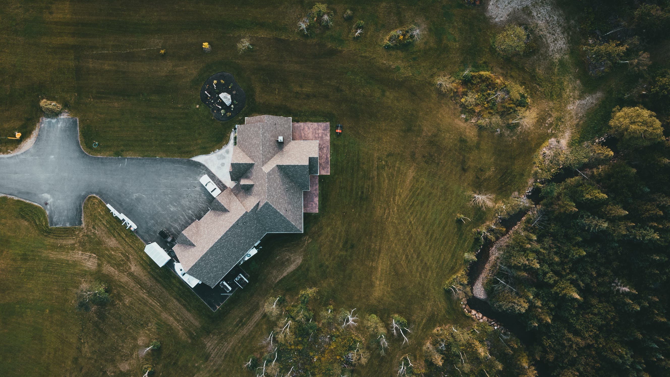 Dronefoto av en enebolig med gårdsplass, omgitt av eng og skog